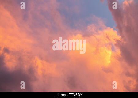 Pink, purple, orange golden glow of clouds at sunset against blue sky Stock Photo