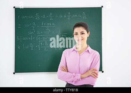 Young female teacher beside blackboard on white background Stock Photo