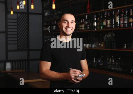 Young handsome waiter with notebook and pen standing in the restaurant Stock Photo
