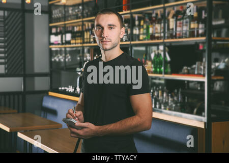 Young handsome waiter with notebook and pen standing in the restaurant Stock Photo
