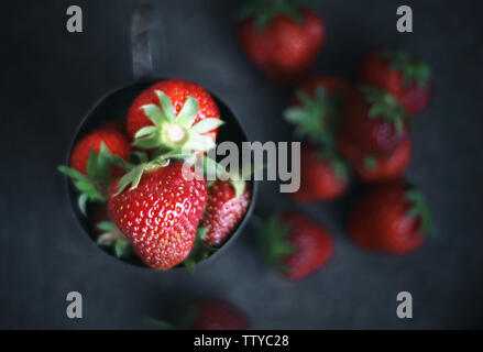 Ripe strawberries scattered around an iron mug. Dark photo Stock Photo
