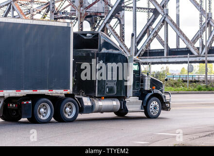 Black stylish big rig classic industrial semi truck with chrome accessories and vertical exhaust pipe transporting commercial cargo in covered black s Stock Photo