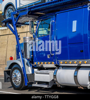 Blue powerful classic big rig car hauler semi truck transporting cars on the special two levels semi trailer running on the road with concrete wall to Stock Photo