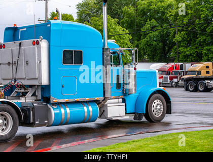 Bright blue classic iconic American big rig long haul professional comfortable powerful semi truck tractor moving on the exit of truck stop to street Stock Photo