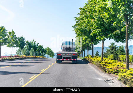 Blue stylish powerful big rig classic industrial semi truck with chrome accessories and vertical exhaust pipe transporting empty flat bed semi trailer Stock Photo