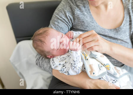 Young Mother feeding milk to a newborn baby. A woman wipes infant face and feeds by a bottle of milk Stock Photo