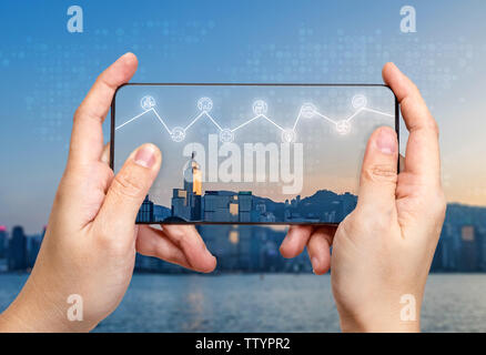Hand holding mobile with Internet of things (iot) word on screen with icon feature glowing in air with blur city building background,Digital Lifestyle Stock Photo