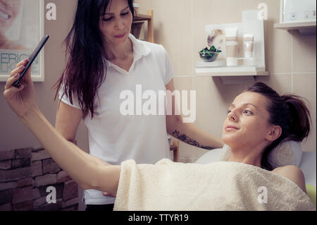 Youn beautiful woman taking selfie at facial mask treatment in beauty salon Stock Photo