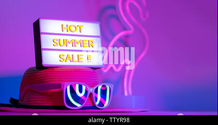 Hot Summer sale in light box on hat with sunglasses refection flamingo neon pink and blue and green light on table with copy space.Trendy vacation hol Stock Photo