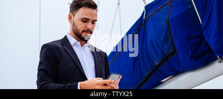 Young handsome businessmen using mobile phone on luxury yacht in bright day Stock Photo