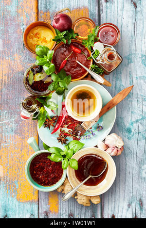 Selection of different sauces and marinades in bowls ready for a BBQ with fresh basil and herbs on a rustic multicolored wood background viewed top do Stock Photo