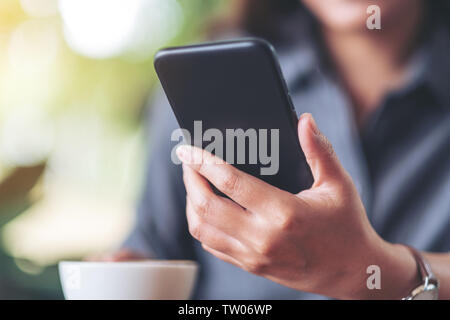 Closeup image of a woman holding  and using mobile phone with coffee cup on wooden table in cafe Stock Photo