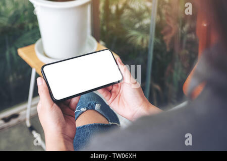 Mockup image of a woman holding and using black mobile phone with blank desktop screen in cafe Stock Photo