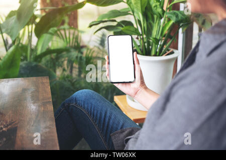 Mockup image of a woman holding and using black mobile phone with blank desktop screen and green nature background Stock Photo