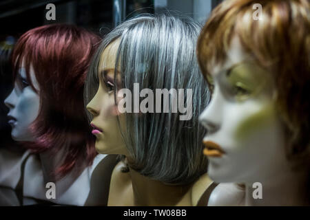 Wigs displayed on mannequin heads in a shop window at night in Poznan, Poland Stock Photo