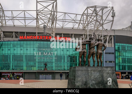 Old Trafford, Manchester, UK - January 20, 2019: Rear view of iconic statue of Best, Law and Charlton with the Manchester United football stadium  in