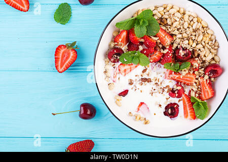 Healthy breakfast - granola, strawberries, cherry, nuts and yogurt in a bowl on a wooden table. Vegetarian concept food. Top view Stock Photo