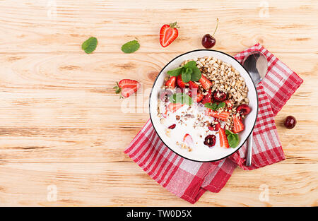 Healthy breakfast - granola, strawberries, cherry, nuts and yogurt in a bowl on a wooden table. Vegetarian concept food. Top view Stock Photo