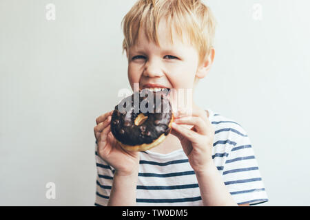 A child boy eats a chocolate donut on a pure white background, real emotions of happiness, lifestyle photography, childish innocence and immediacy. Stock Photo
