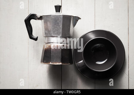 Vintage Italian moka pot lay on white wooden table near black empty cup, top view Stock Photo