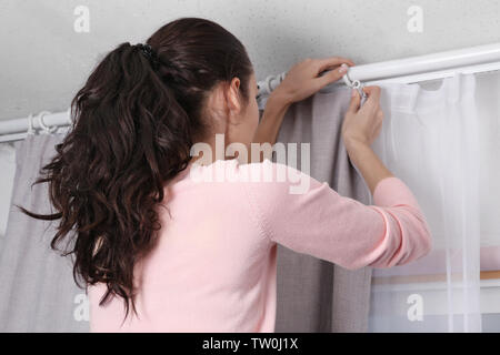 Young woman installing curtains over window Stock Photo