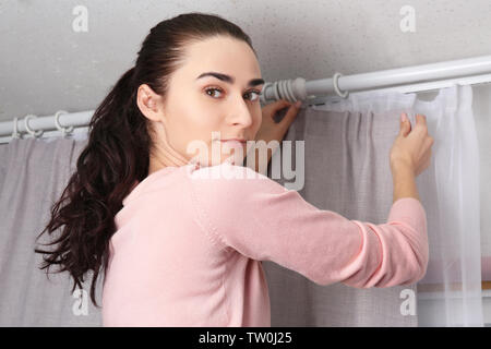 Young woman installing curtains over window Stock Photo