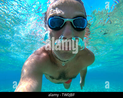 Underwater view of a young diver man swimming in the sea. Air bubbles coming out from mouth and nose Stock Photo