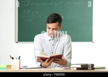 Handsome young teacher sitting at table in classroom Stock Photo