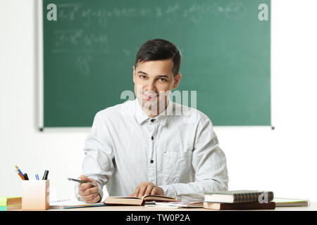 Handsome young teacher sitting at table in classroom Stock Photo