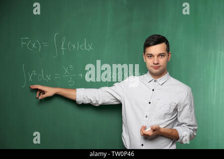 Handsome young teacher explaining math formulas written on blackboard Stock Photo