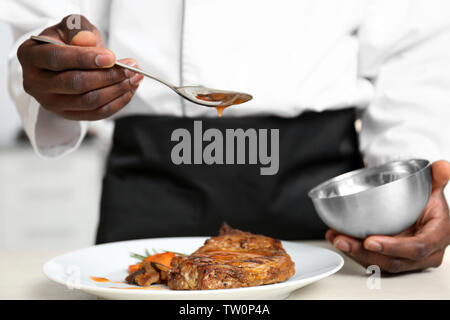 African American chef pouring sauce on tasty meat in kitchen, closeup Stock Photo