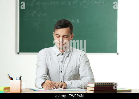 Handsome young teacher sitting at table in classroom Stock Photo