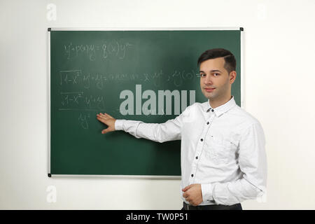Handsome young teacher explaining math formulas written on blackboard Stock Photo
