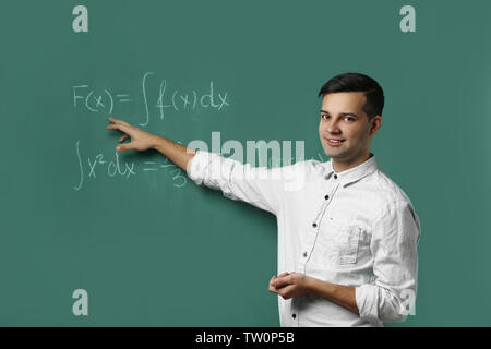 Handsome young teacher explaining math formulas written on blackboard Stock Photo