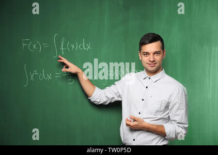 Handsome young teacher explaining math formulas written on blackboard Stock Photo