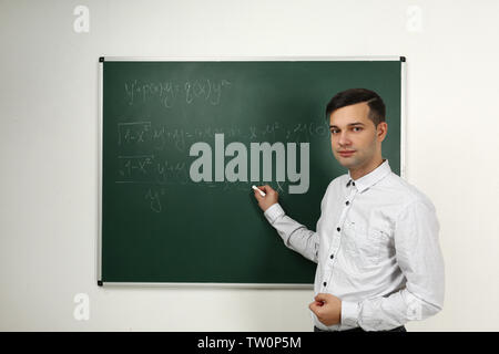 Handsome young teacher explaining math formulas written on blackboard Stock Photo