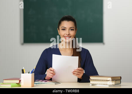 Beautiful young teacher sitting at table in classroom Stock Photo