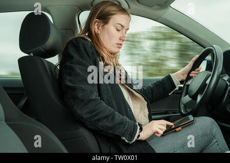 A young woman is typing on a mobile while driving a car Stock Photo