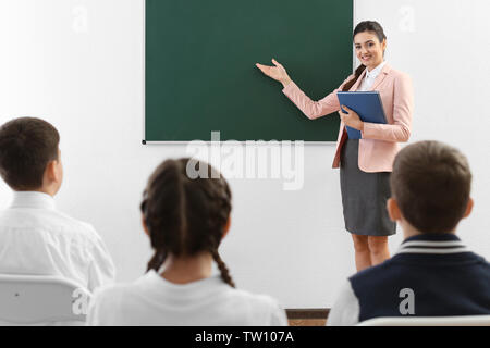 Teacher explaining new topic while standing near blackboard in classroom Stock Photo