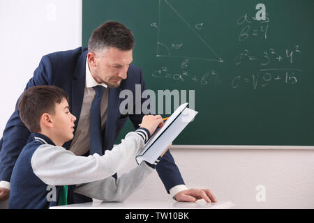Male teacher and schoolboy doing task in classroom Stock Photo