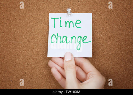 Female hand holding note with phrase TIME CHANGE on cork board background Stock Photo