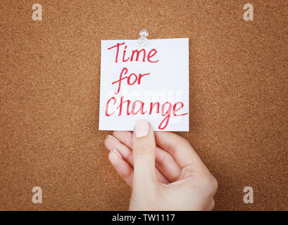 Female hand holding note with phrase TIME FOR CHANGE on cork board background Stock Photo