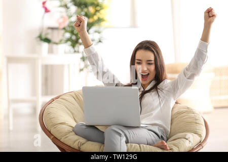 Young woman with laptop sitting on armchair at home Stock Photo