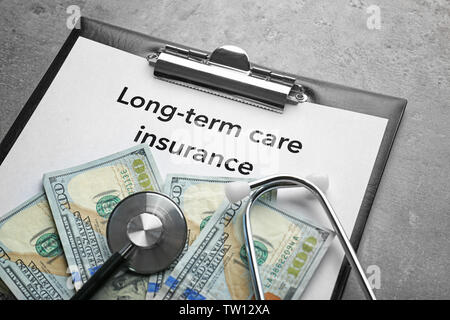 Text LONG-TERM CARE INSURANCE on clipboard with stethoscope and dollars closeup Stock Photo