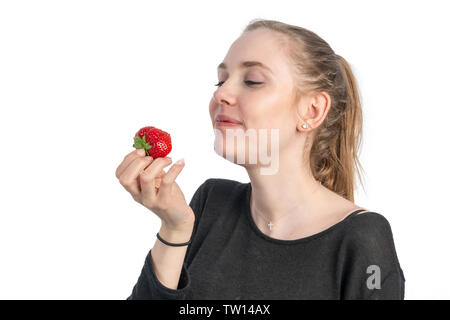 A young smiling woman enjoys eating a strawberry Stock Photo