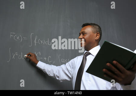 Confident Indian teacher writing math formulas on blackboard Stock Photo