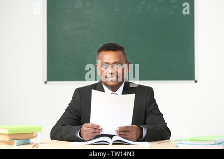 Confident Indian teacher sitting at table in classroom Stock Photo