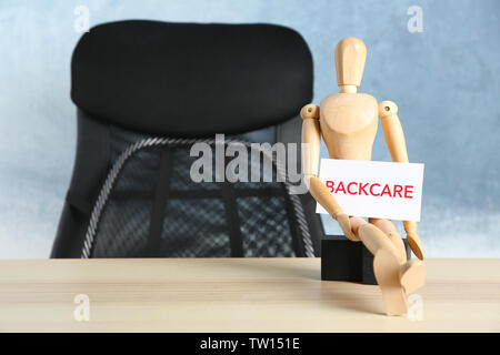 Wooden mannequin sitting on table and holding paper with word BACKCARE Stock Photo