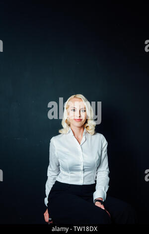 Studio portrait of an attractive blond business woman in a white shirt and black pants against plain background Stock Photo