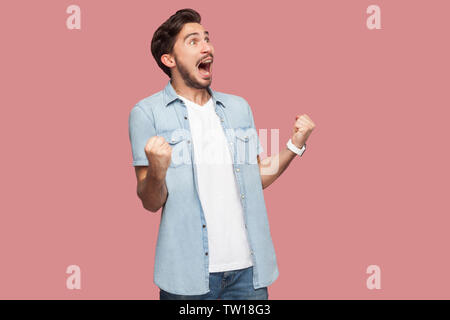 Portrait of happy screaming handsome bearded young man in blue casual style shirt standing with suprised face and rejoicing his victory. indoor studio Stock Photo